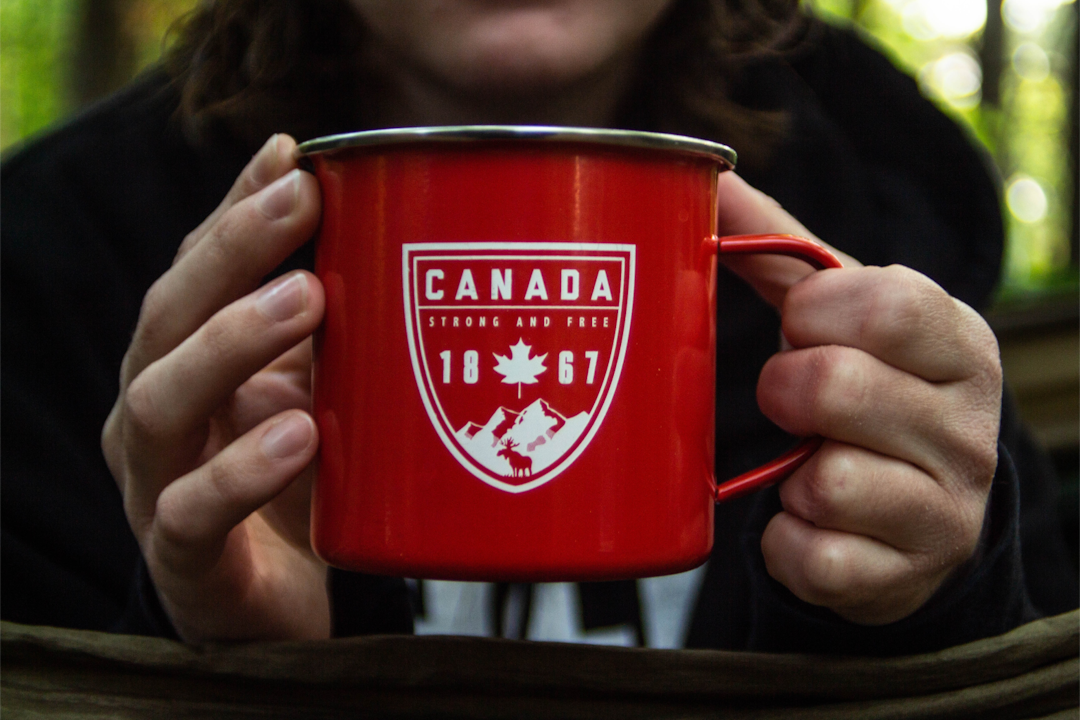 A closeup of a person's hands holding a red mug with a graphic that reads: Canada - 1867.